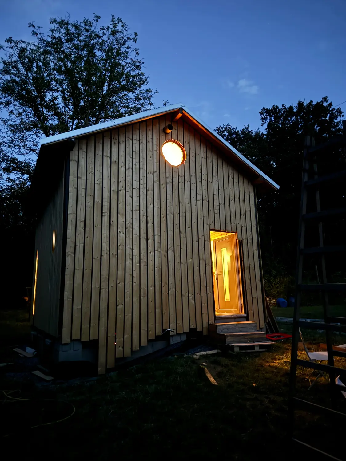 Dřevostavba večer s rozsvíceným oknem a světlem nad dveřmi