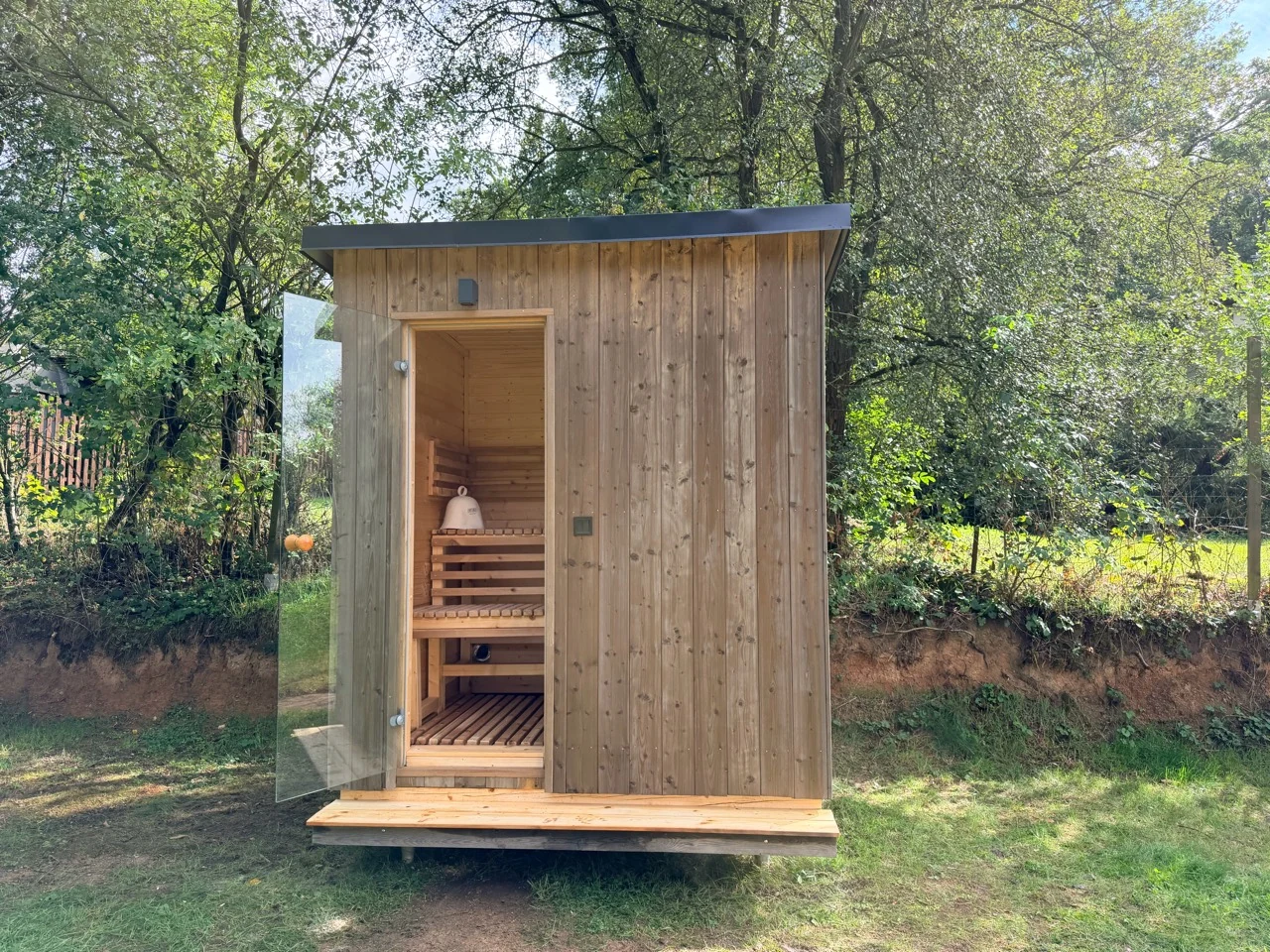 Venkovní sauna se svislým obkladem a prosklenými dveřmi na zahradě